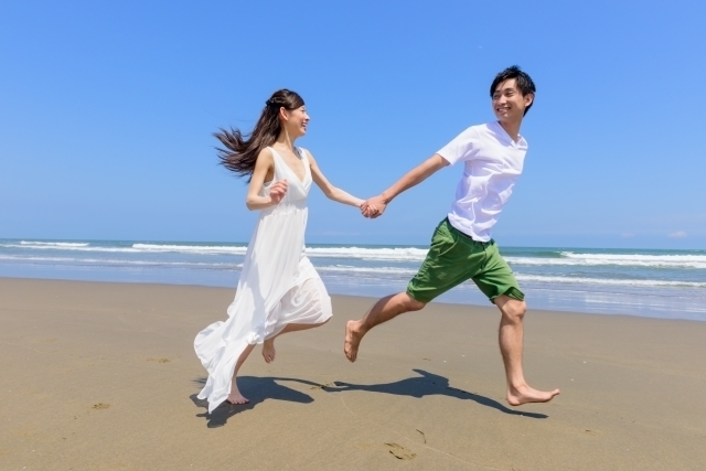 手を繋いで海辺を走るカップルの画像